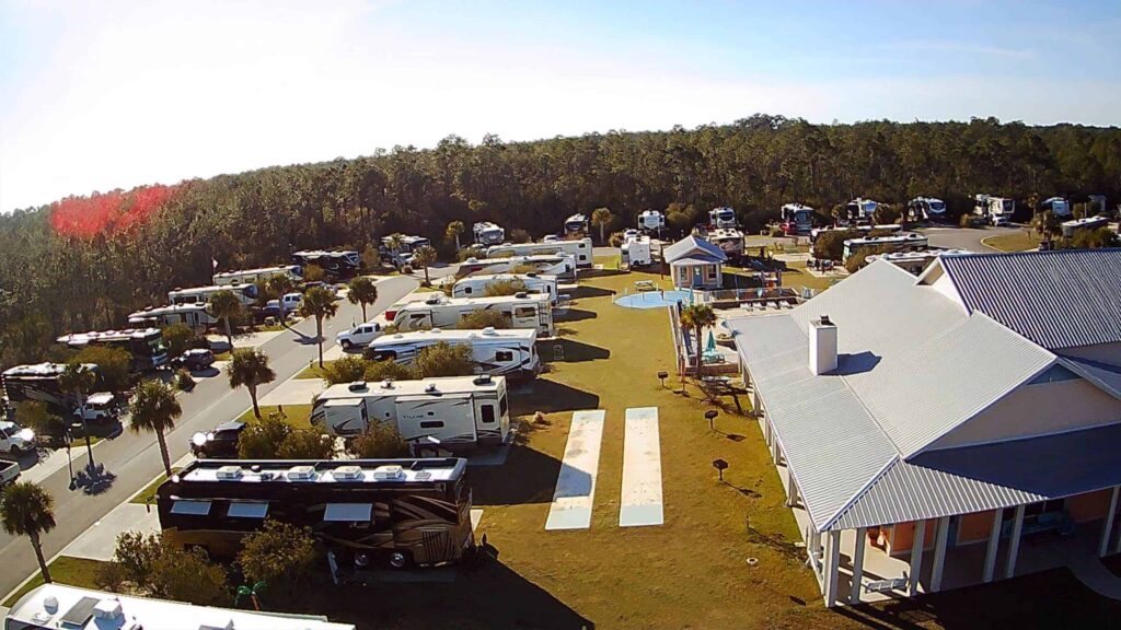 Aerial shot of a clubhouse and RV sites, with pal trees and pool visible