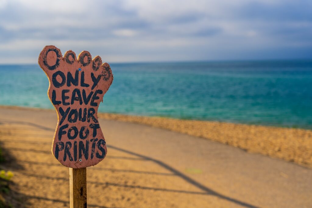 a sign in the shape of a foot that reads only leave your for prints. Appears next to a sidewalk and water in the background.