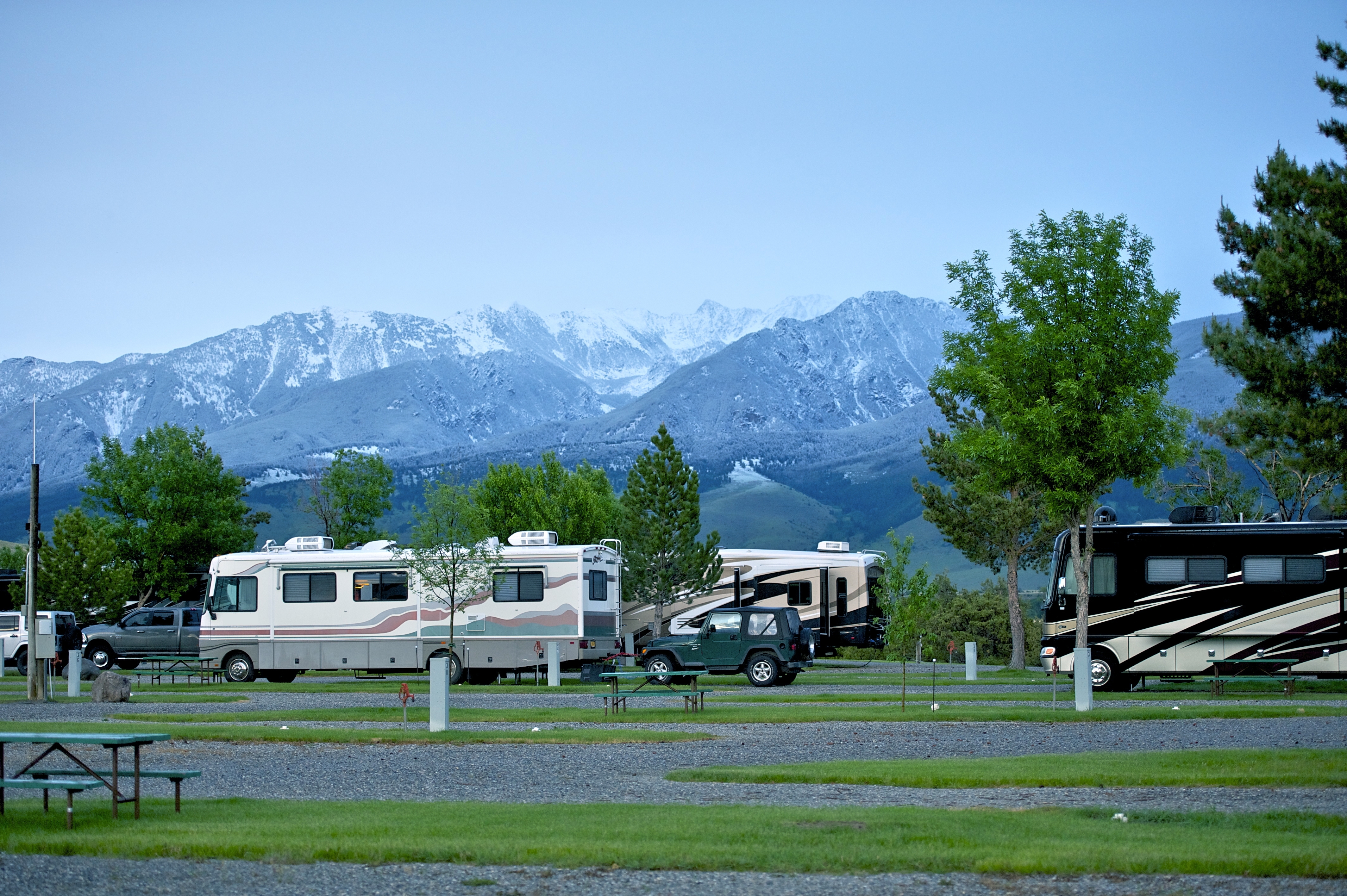 RV park with grass and cement pads. There are snow capped mountains in the background.