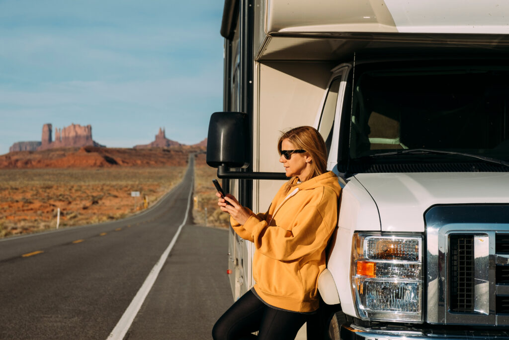 woman standing outside in the american west leaning on rv looking at cell phone